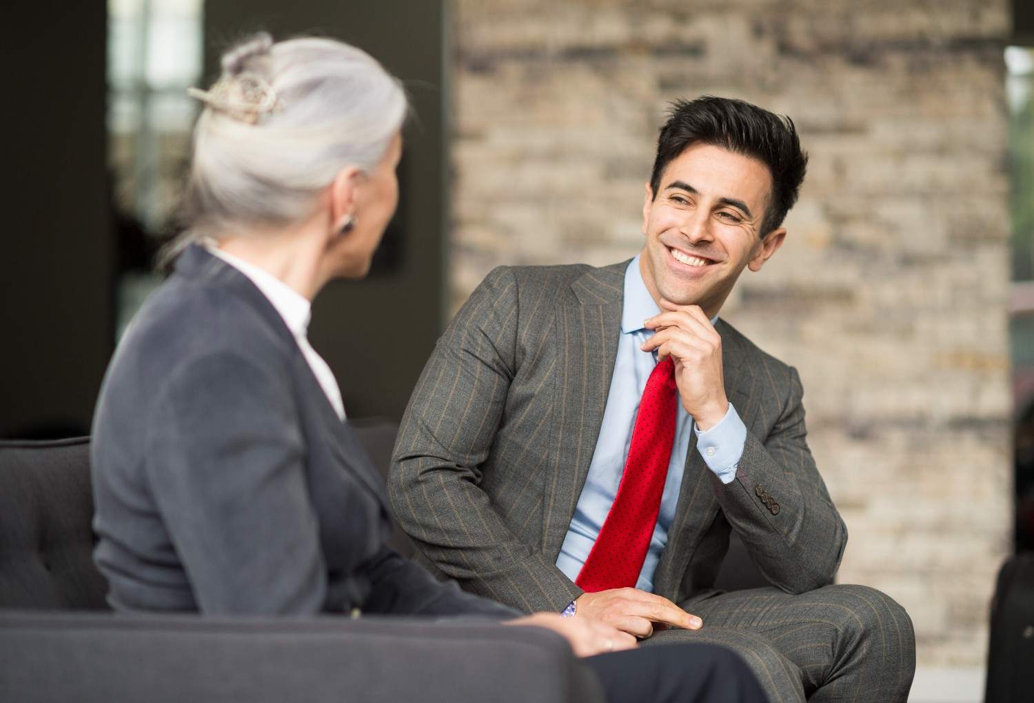 A real estate agent in a suit attentively speaking with a client in a modern office, smiling and engaged in a one-on-one conversation.