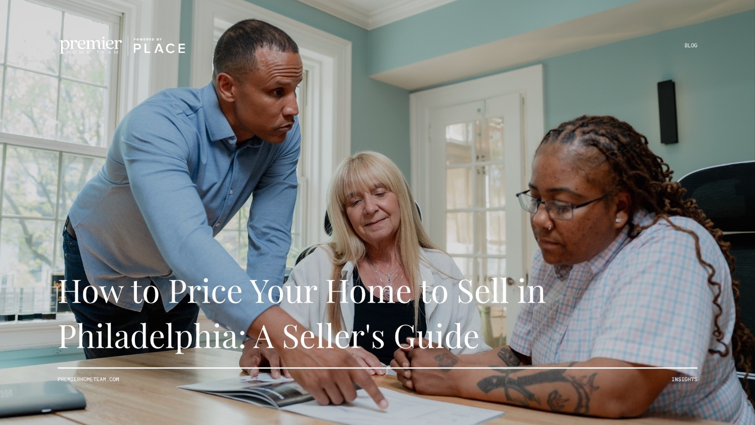 A real estate blog header image featuring a full-width photo background with a dark overlay. The scene shows three people gathered around a wooden table in a brightly lit room with large windows. A Black man in a blue button-down shirt leans forward, pointing at an open booklet on the table. A blonde woman sits next to him, looking down attentively, while a Black woman with glasses and tattoos on her arm listens carefully on the right. Bold white serif text overlaid across the bottom reads, 