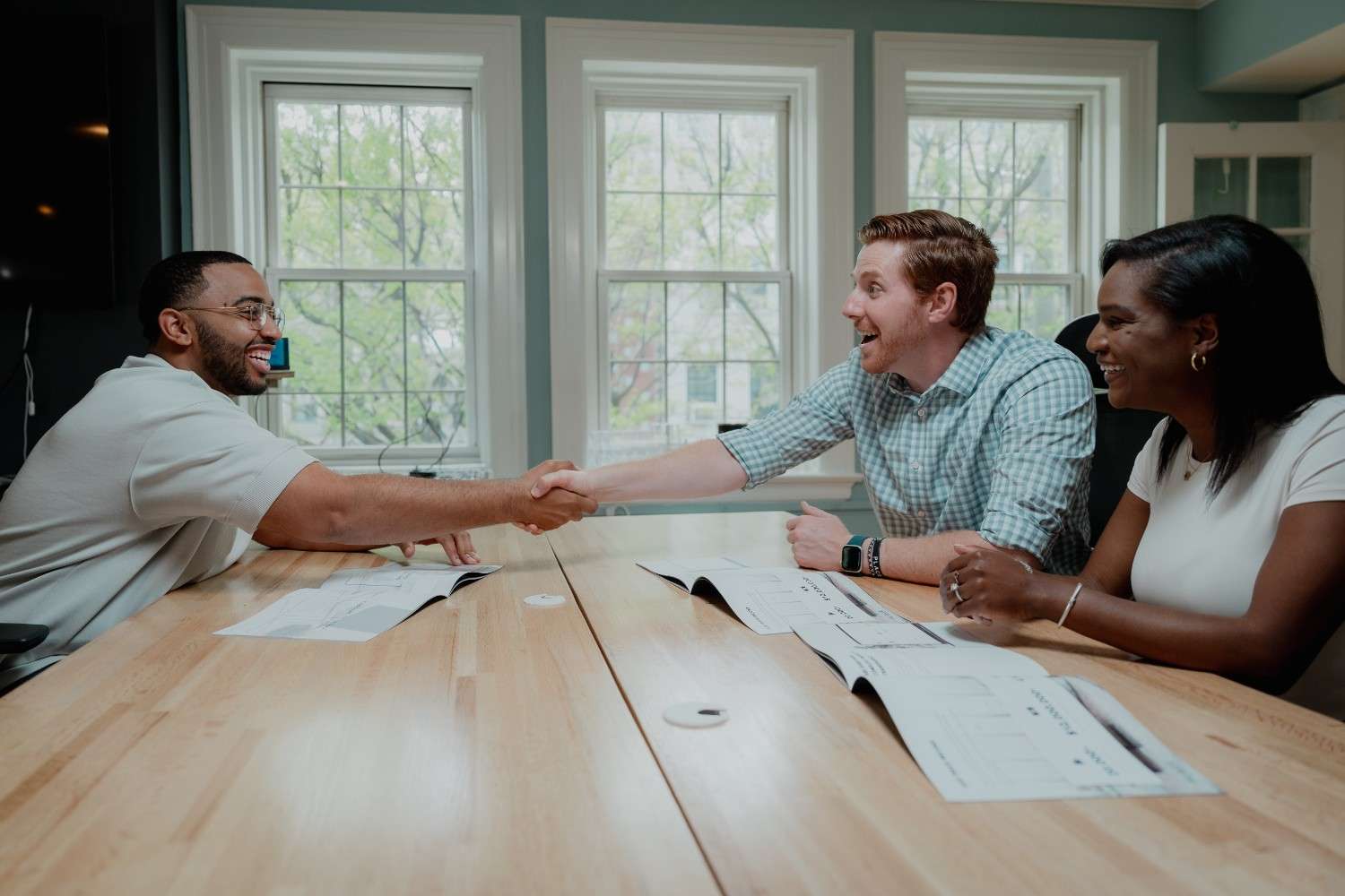 Real estate agent meeting with home buyers at a table, reviewing documents and shaking hands
