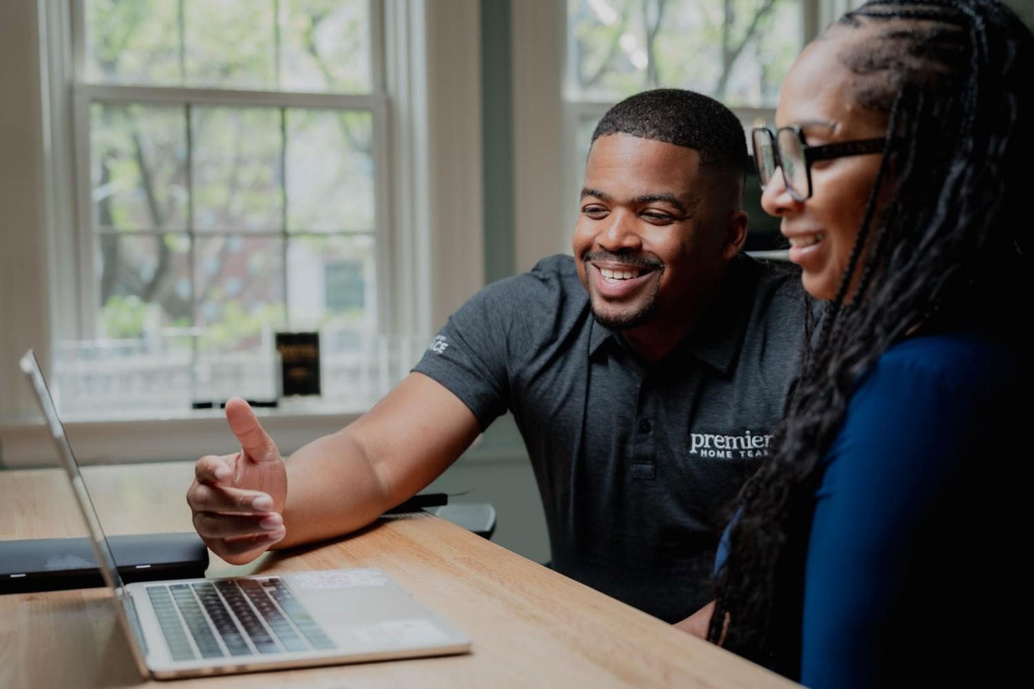 A smiling Premier Home Team real estate agent reviewing property listings on a laptop with a client during a home buyer consultation.