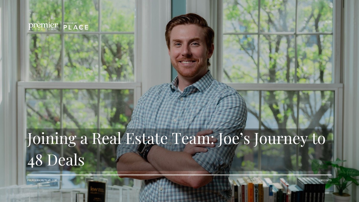 A real estate agent recruiting blog header image utilizing a full-width photo background with a subtle dark overlay. The scene features a smiling white man with red hair, wearing a green and white plaid shirt, standing with his arms crossed in front of a large window looking out onto green trees. Bold white serif text overlaid across the bottom reads, 