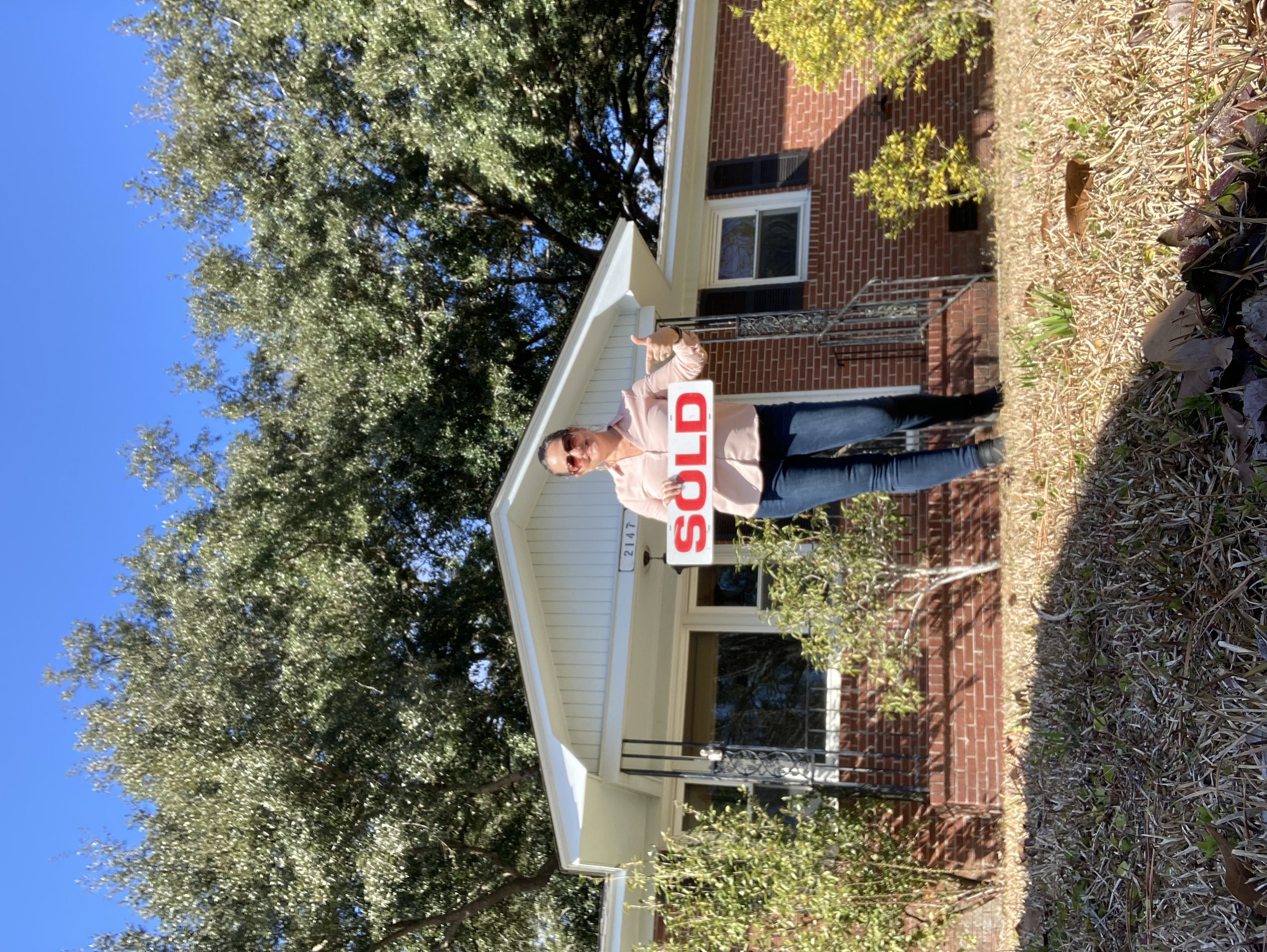 Stephanie Davis with a sold sign in front of a brick house