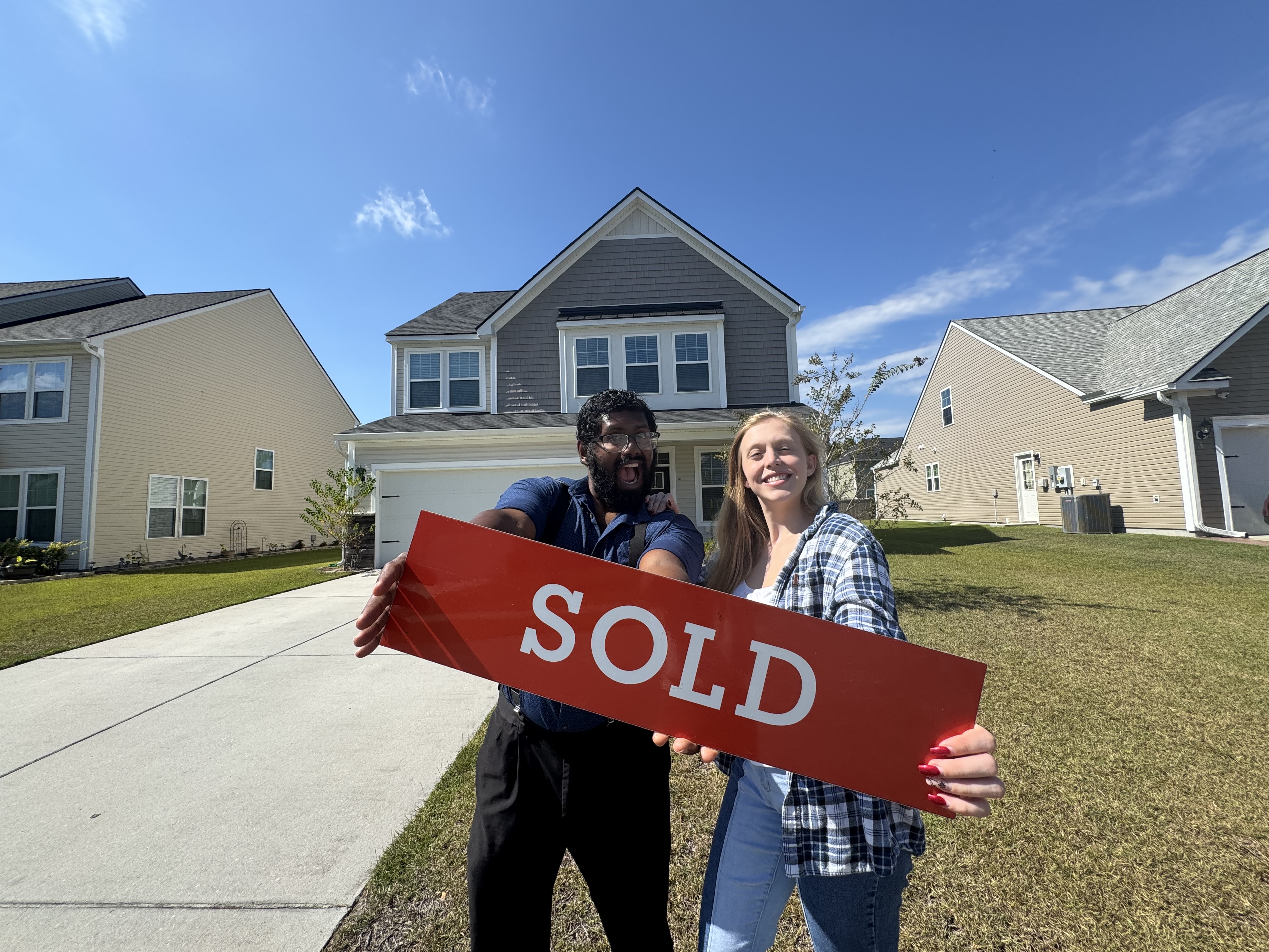 Couple holding sold sign in front of their new home