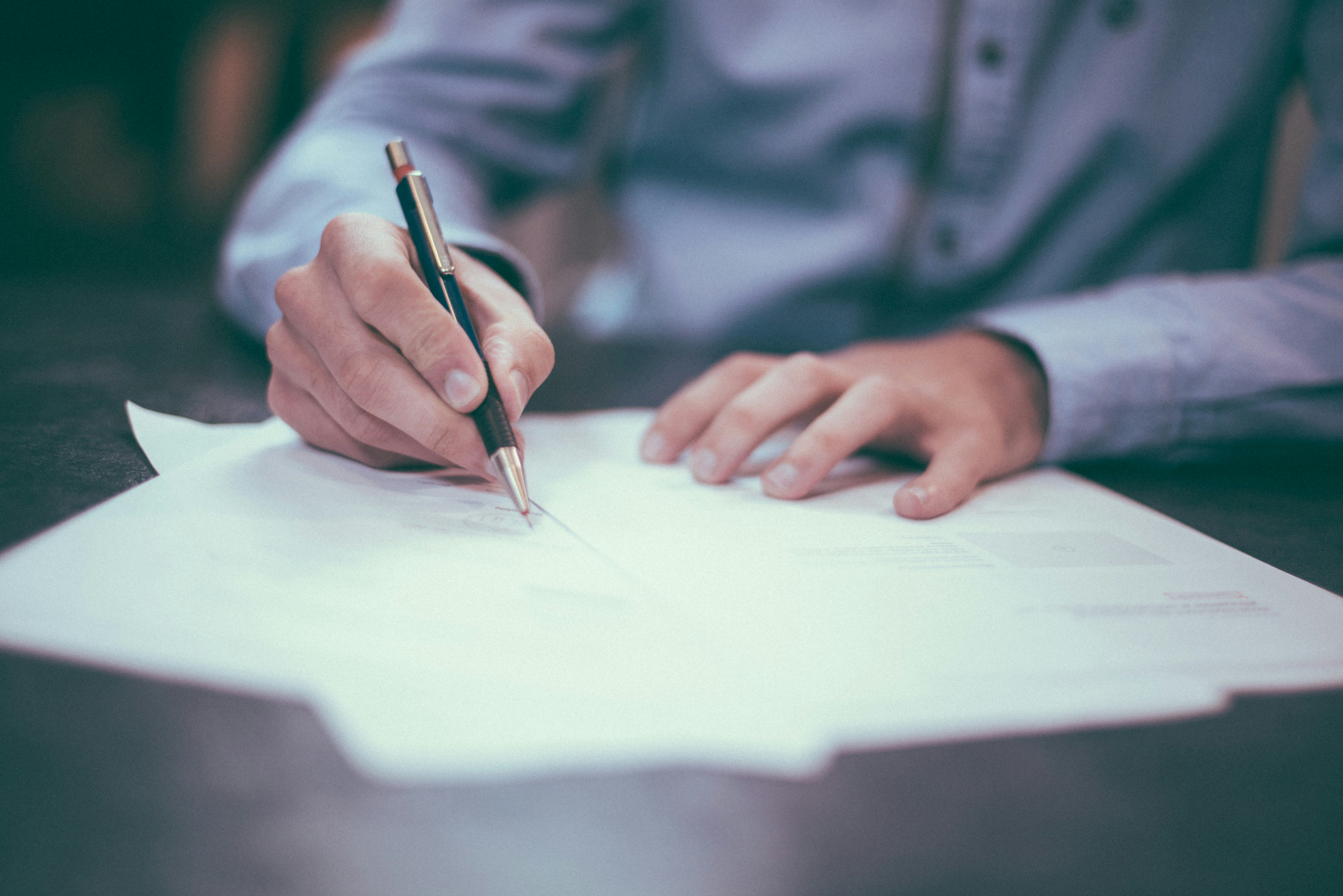 Person signing real estate documents with a pen on a desk, symbolizing Texas Seller’s Disclosure and T-47 forms