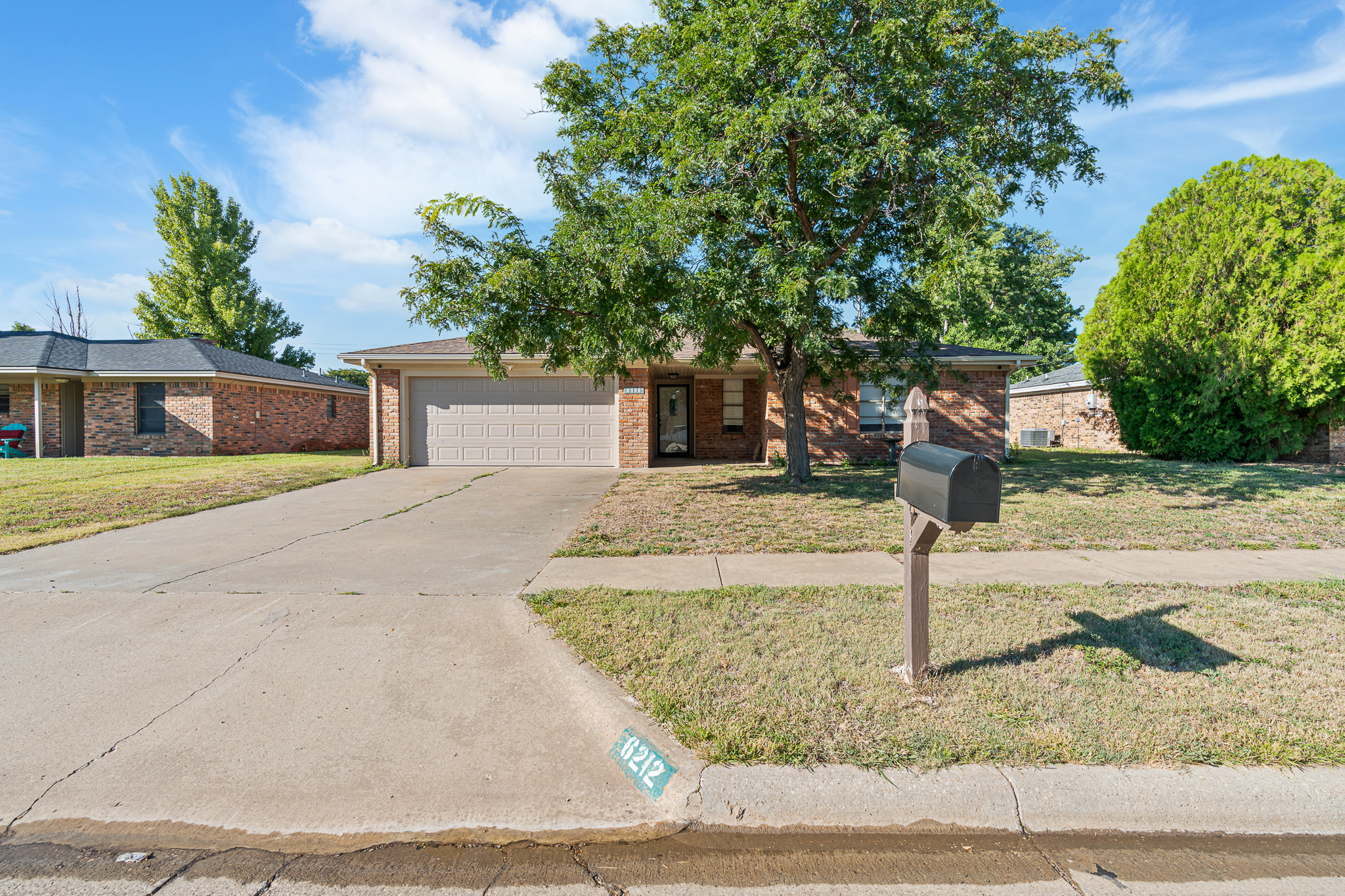 Front view of 6212 Rutgers Street, Amarillo TX 79109 — single-story brick home with attached two-car garage, mature tree, and driveway