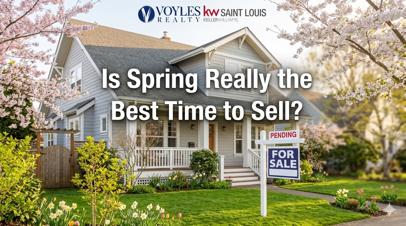 A bright, airy photograph of a beautiful two-story light blue house in the spring, featuring blooming cherry blossom trees and a green lawn with daffodils. A 'For Sale' sign with a 'Pending' rider stands in the foreground. Centered at the top is the Voyles Realty KW Saint Louis logo. Large, bold white text in the center reads: 'Is Spring Really the Best Time to Sell?