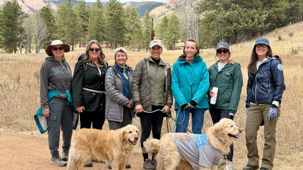 A group of ladies behind the Colorado scenery on a nature hike with two golden retrievers