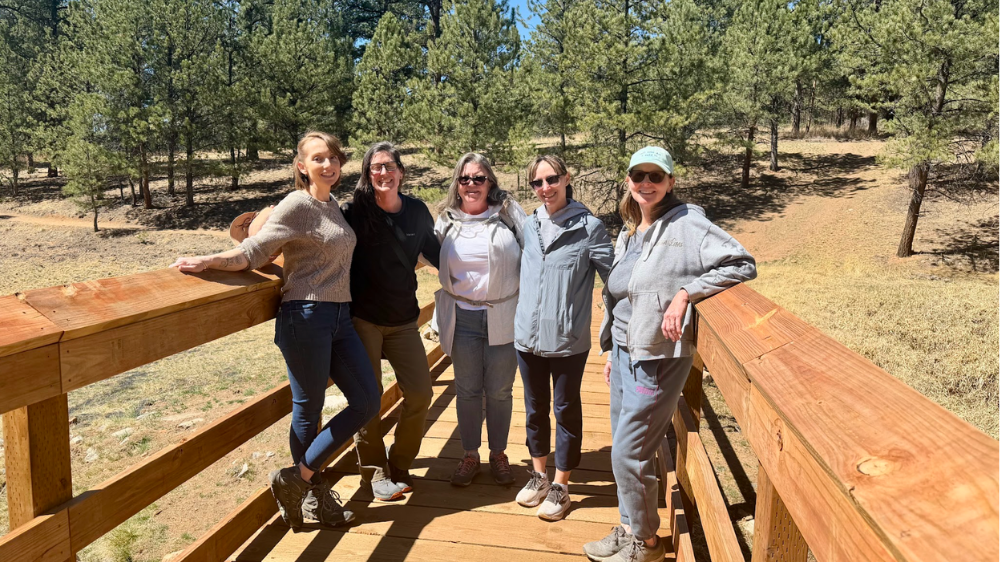 A group of Colorado ladies smiling standing on a bridge in a Colorado park