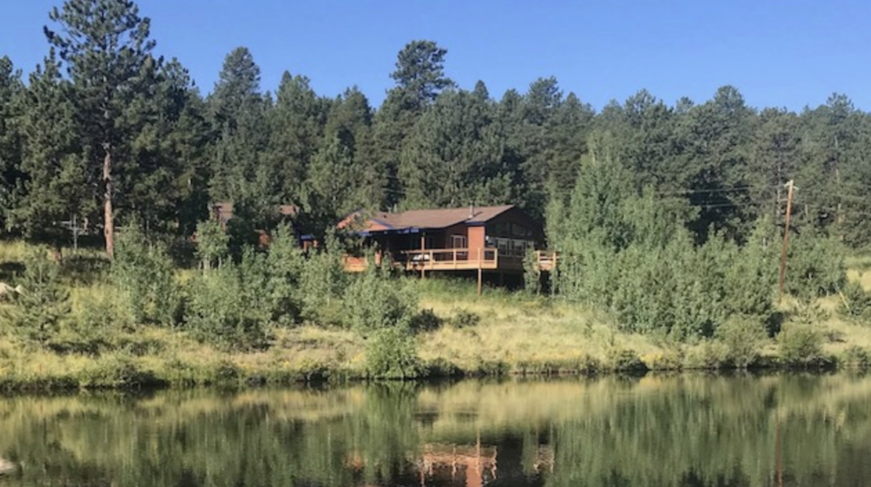 A Colorado home over a lake hidden in a green forest.
