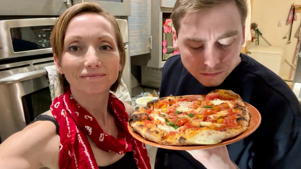 Victoria and her husband posing in front of a homemade pizza