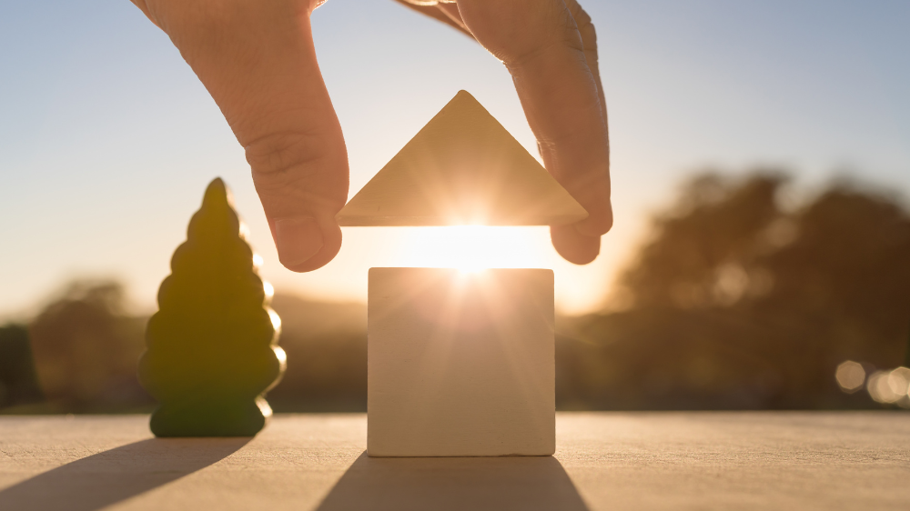 A hand putting together a wooden house to represent the psychology of sorting your house