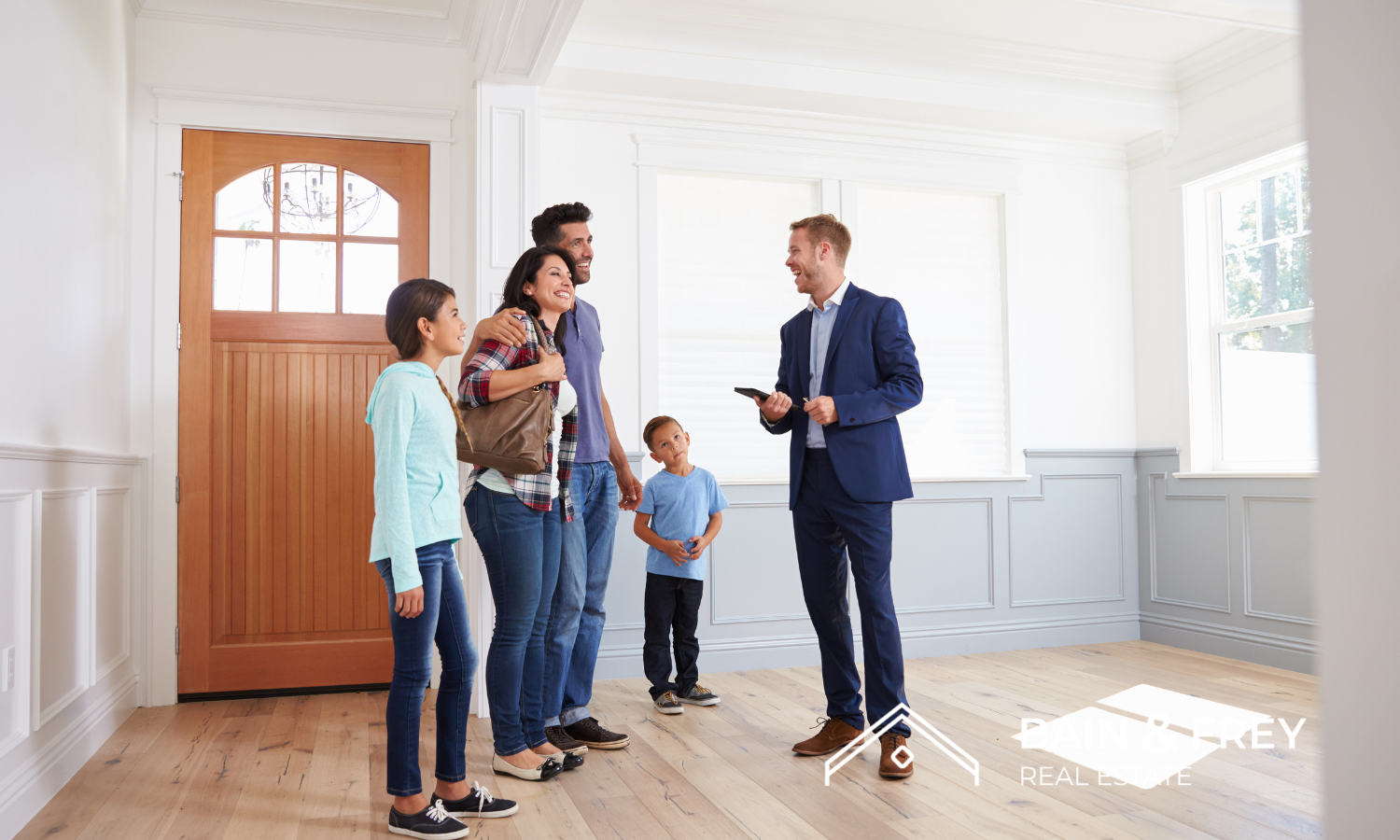 Smiling family viewing an empty home with their Bain & Frey Real Estate agent in a light-filled modern entryway. 