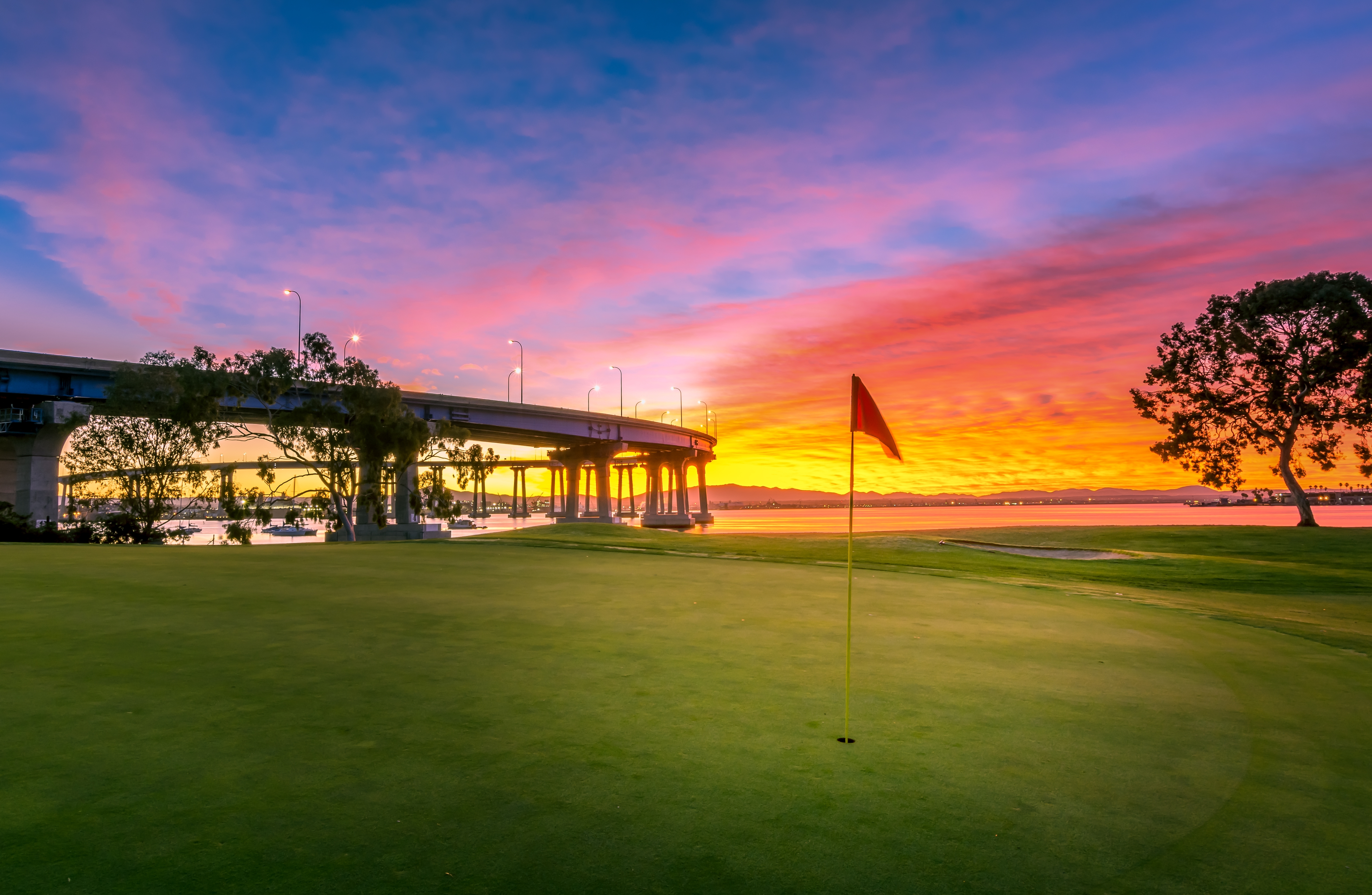 Coronado golf course with a flag in the foreground, the bridge in the background and a sunset