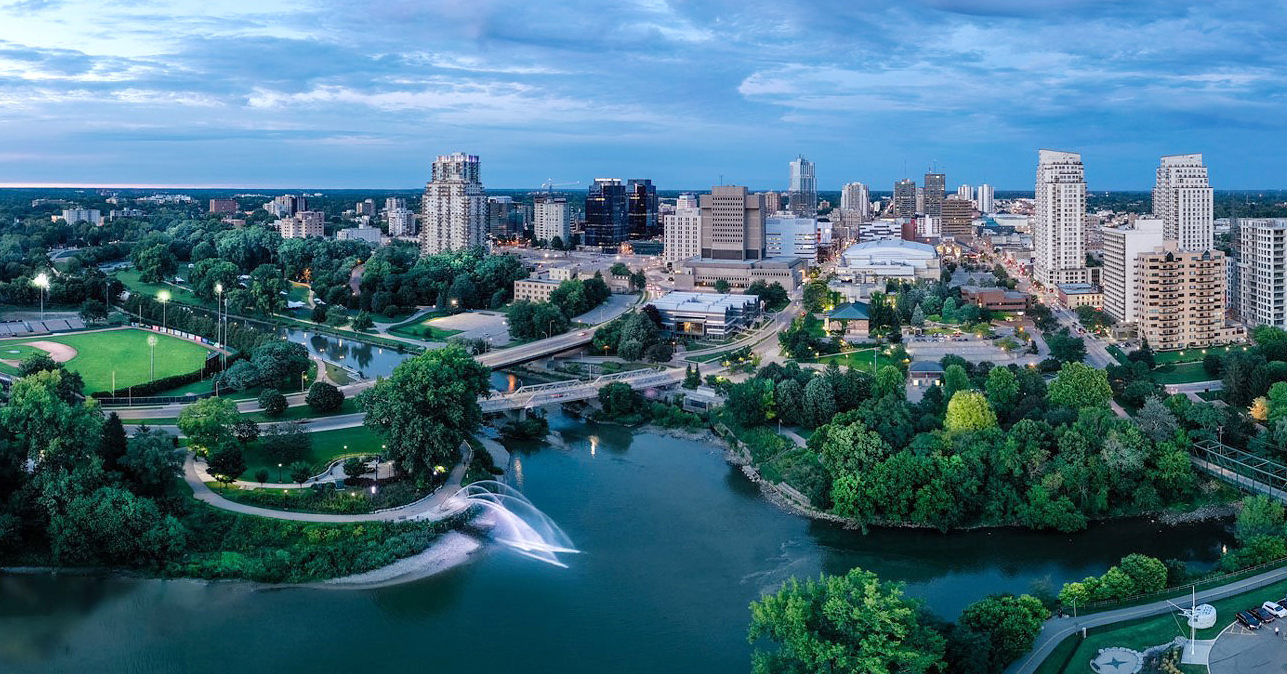  An aerial panoramic view of the London, Ontario skyline at dusk, showcasing the intersection of the Thames River. The image captures the 