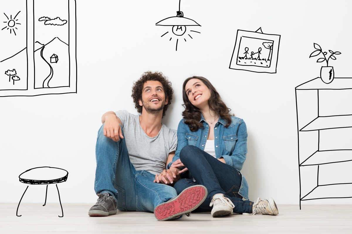  A young couple sits on the floor of a minimalist room, leaning against a white wall decorated with whimsical line drawings of home furniture and a window view, symbolizing their dreams of first-time homeownership.