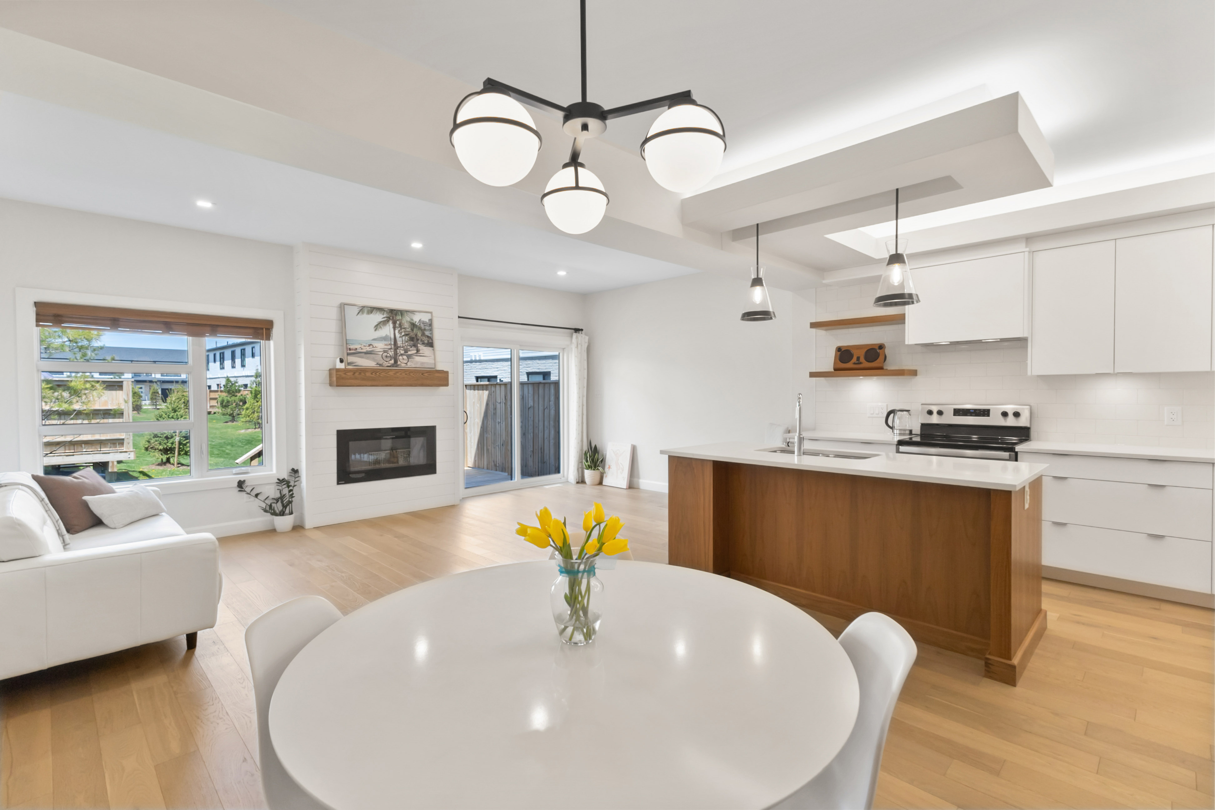 Bright and modern open-concept main floor in a London, Ontario home, featuring a white kitchen with a wooden island, a dining table with yellow flowers, and a cozy living area with a fireplace.