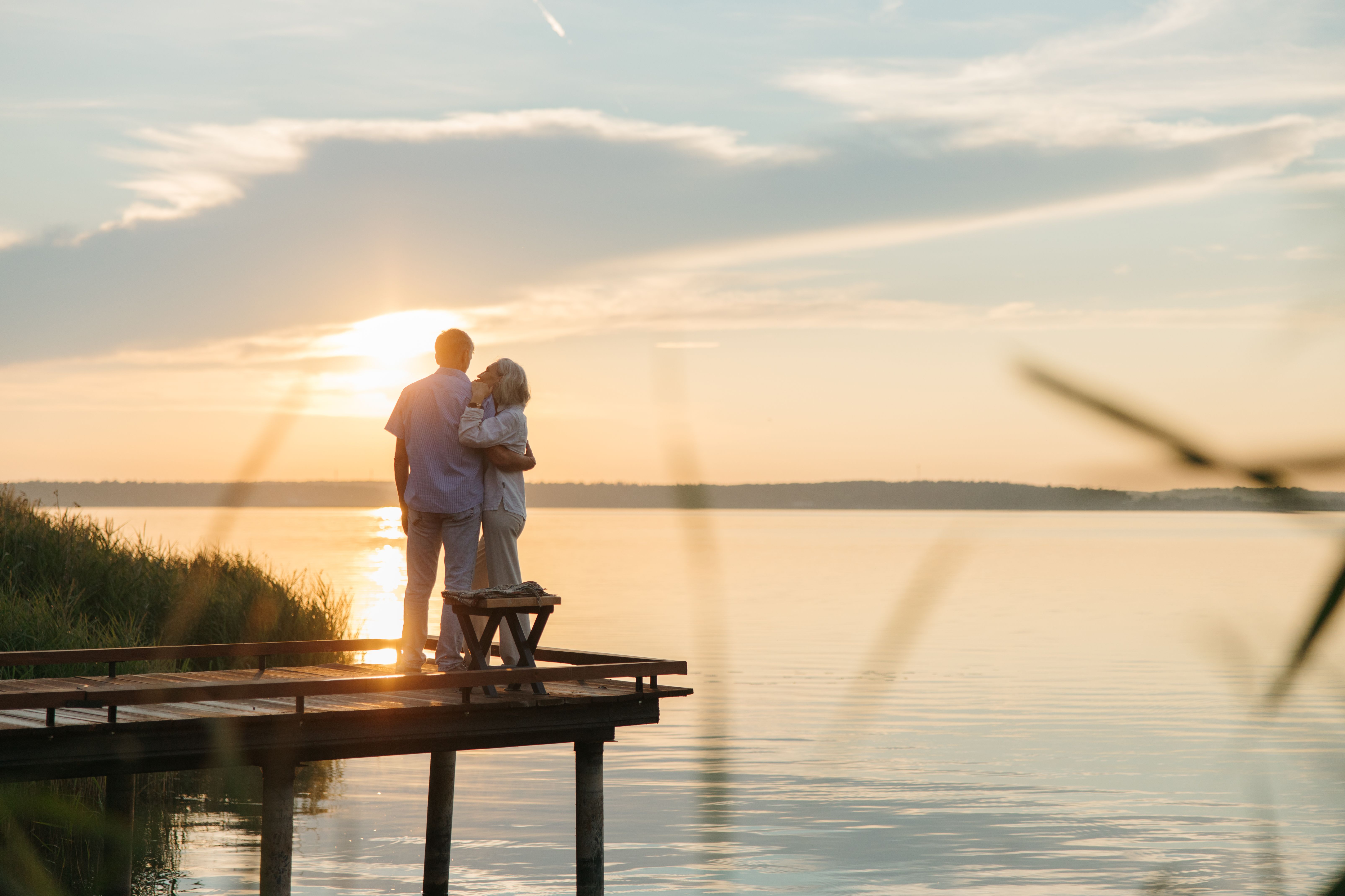Happy retired couple enjoying waterfront living in Punta Gorda, Florida, watching sunset over Charlotte Harbor from a dock with tropical landscaping. 