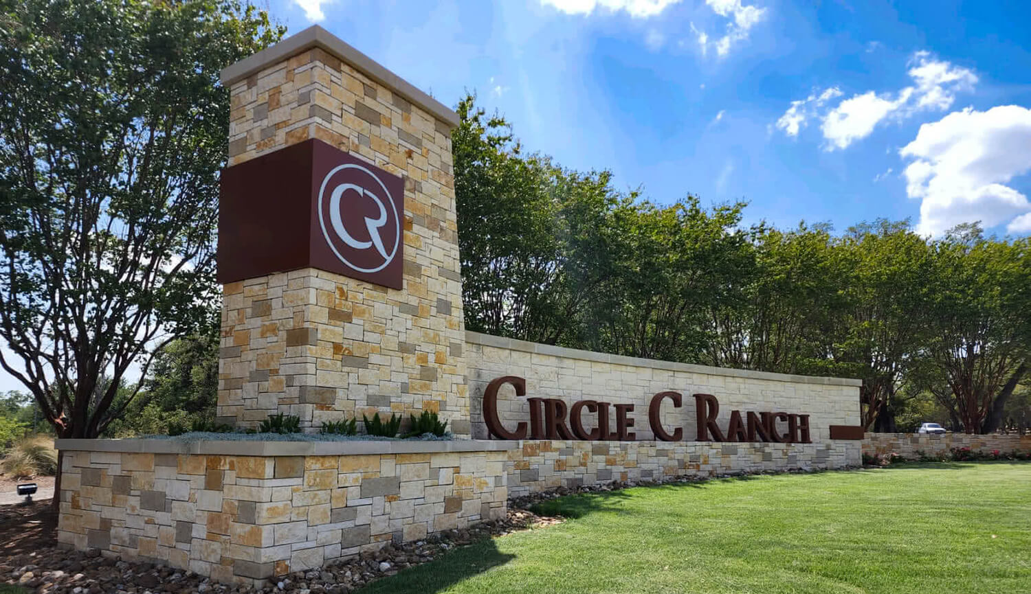 Entrance sign for Circle C Ranch in Southwest Austin, Texas featuring stone monument, landscaped greenery, and blue sky in a popular family-friendly master-planned community