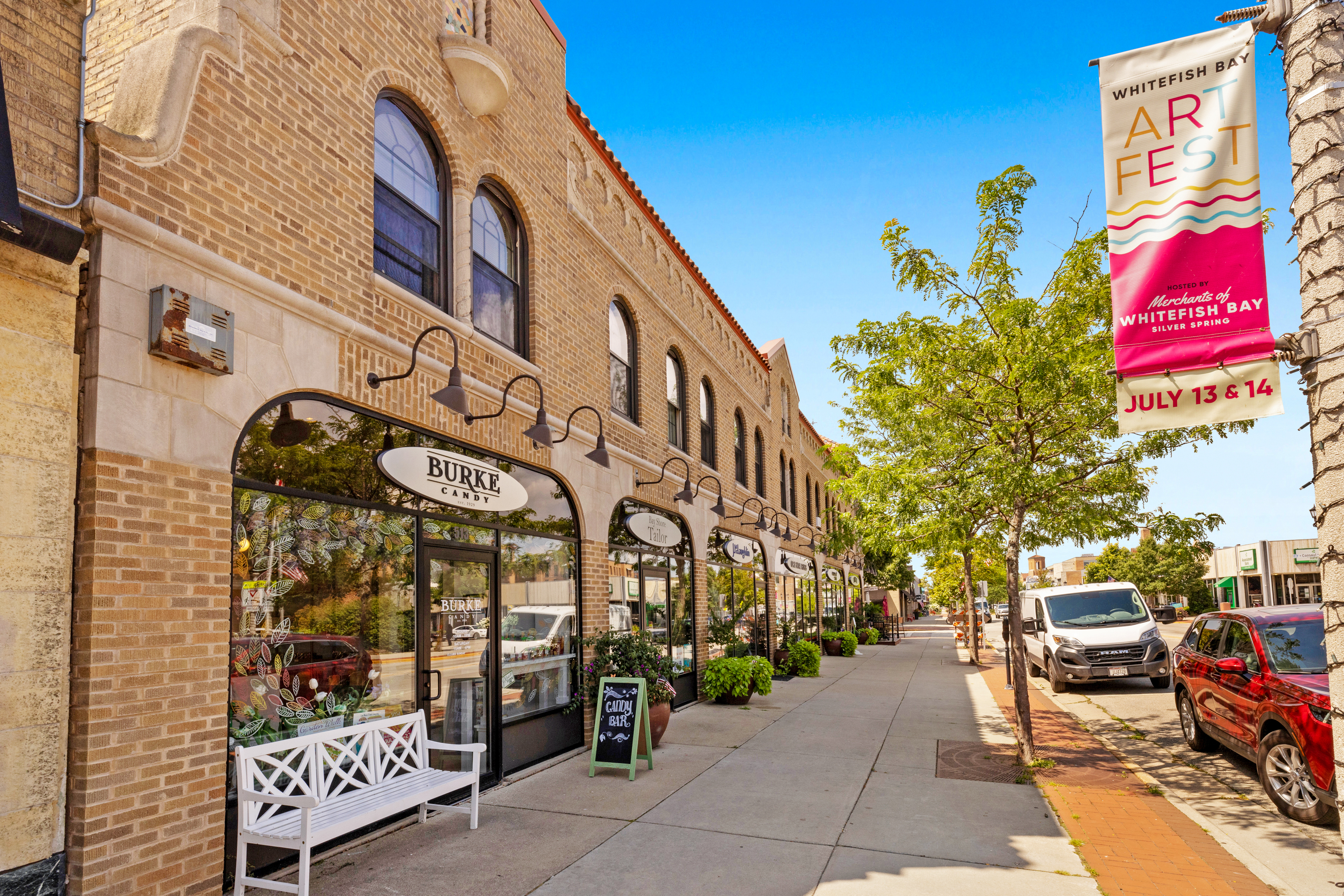 Tree-lined sidewalk with brick storefronts and local shops in a Milwaukee-area neighborhood