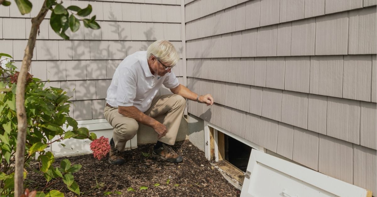 A home inspector examining a crawl space vent on the exterior of a house during a home inspection in Eau Claire, Wisconsin.