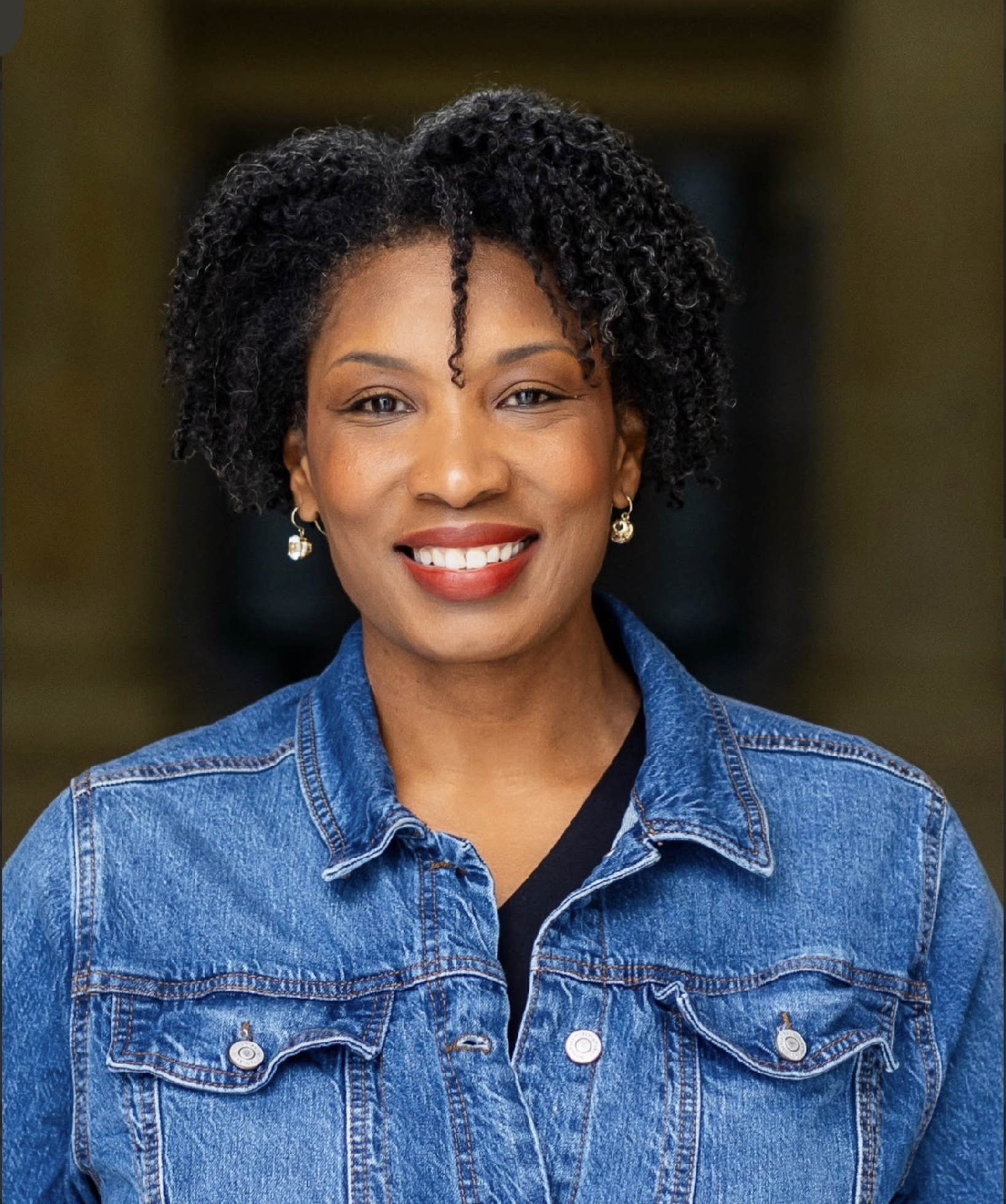 black woman with red lipstick in a jean jacket smiling