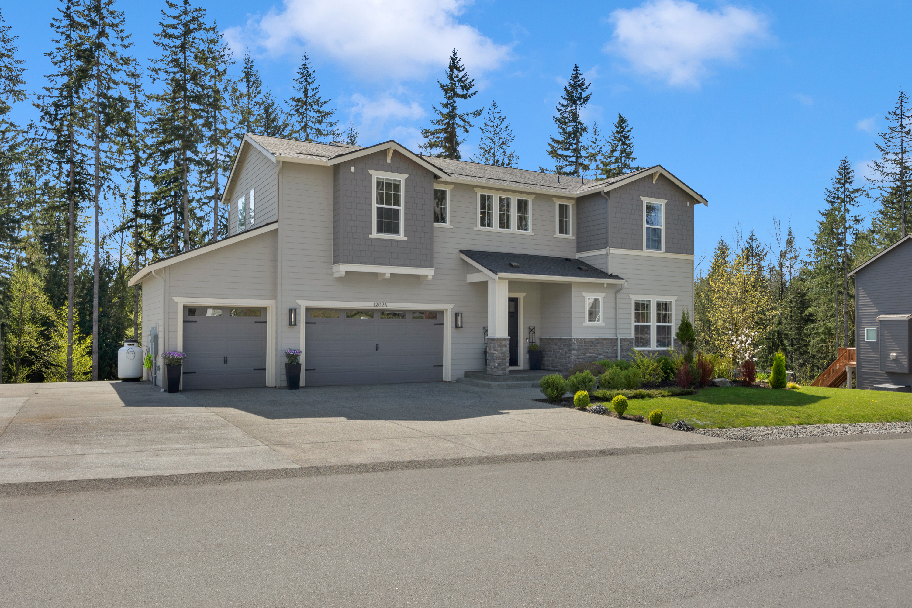 Exterior view of a spacious 5-bedroom home in Lake Stevens' Glenmore community, showcasing a large driveway and private wooded backdrop.