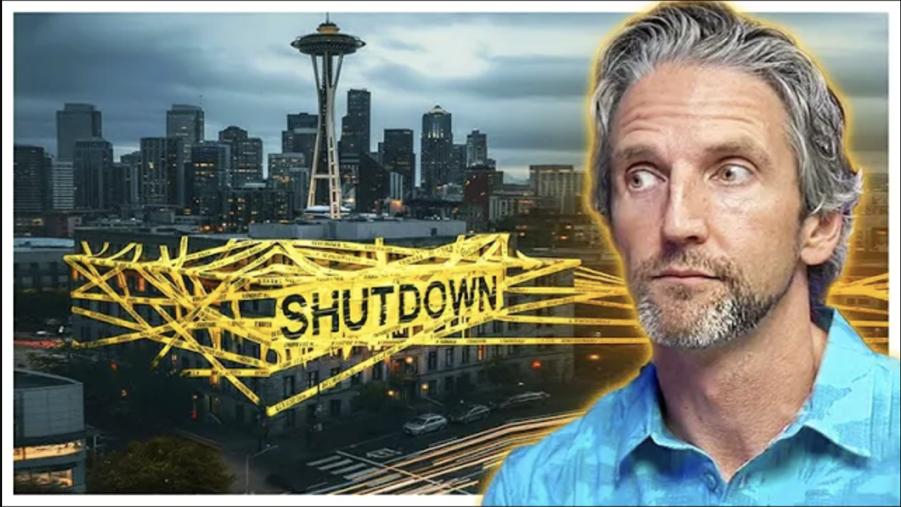 A man with a concerned expression standing in front of the Seattle skyline while a building is wrapped in bright yellow shutdown tape and the Space Needle rises in the background.