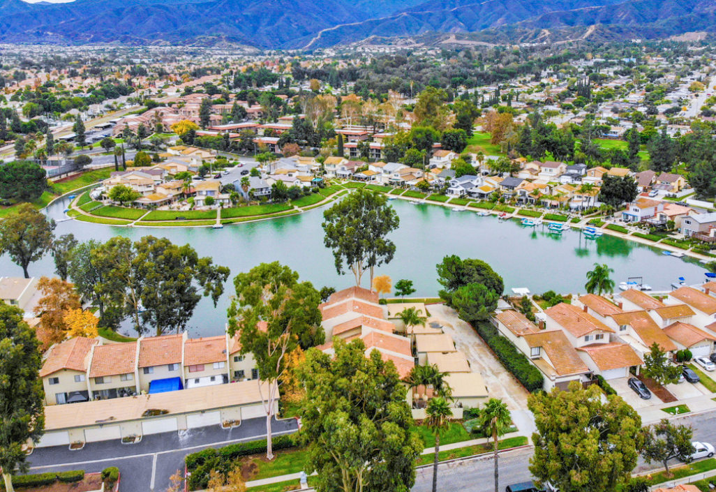 Aerial view of a residential neighborhood in Corona, California with homes surrounding a lake and mountains in the background.