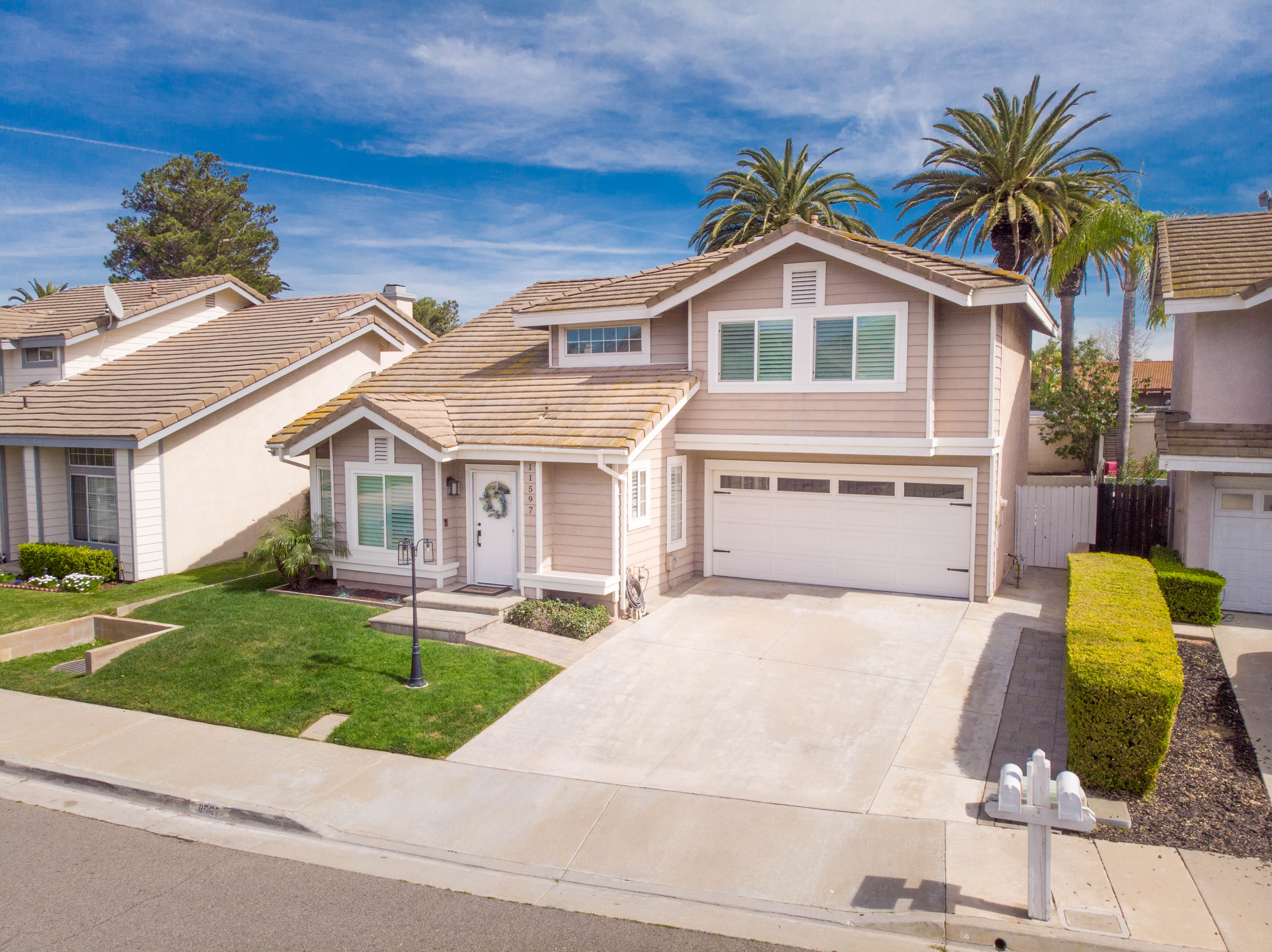 Front exterior of 11597 Norgate Drive, Corona CA, featuring a two-story beige home with attached two-story garage, green front lawn, and palm trees in the background.