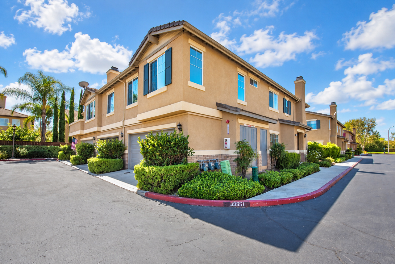 Exterior view of the Villas at Old School House community in Murrieta featuring two-story stucco homes, mature landscaping and palm trees.