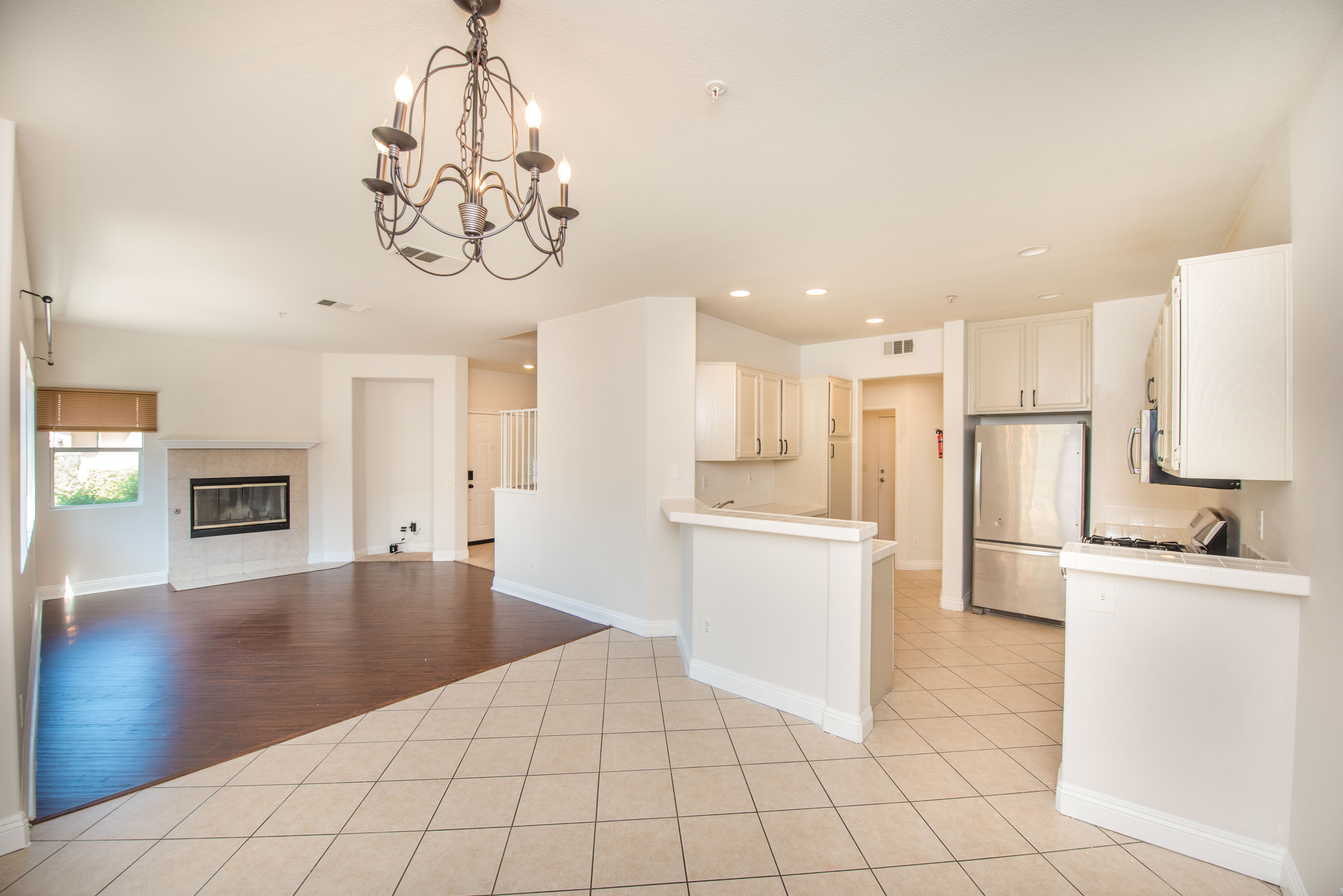 Open kitchen and living area at 39951 Millbrook Way #B in Murrieta with white cabinetry, breakfast bar, tile flooring, natural light and fireplace.