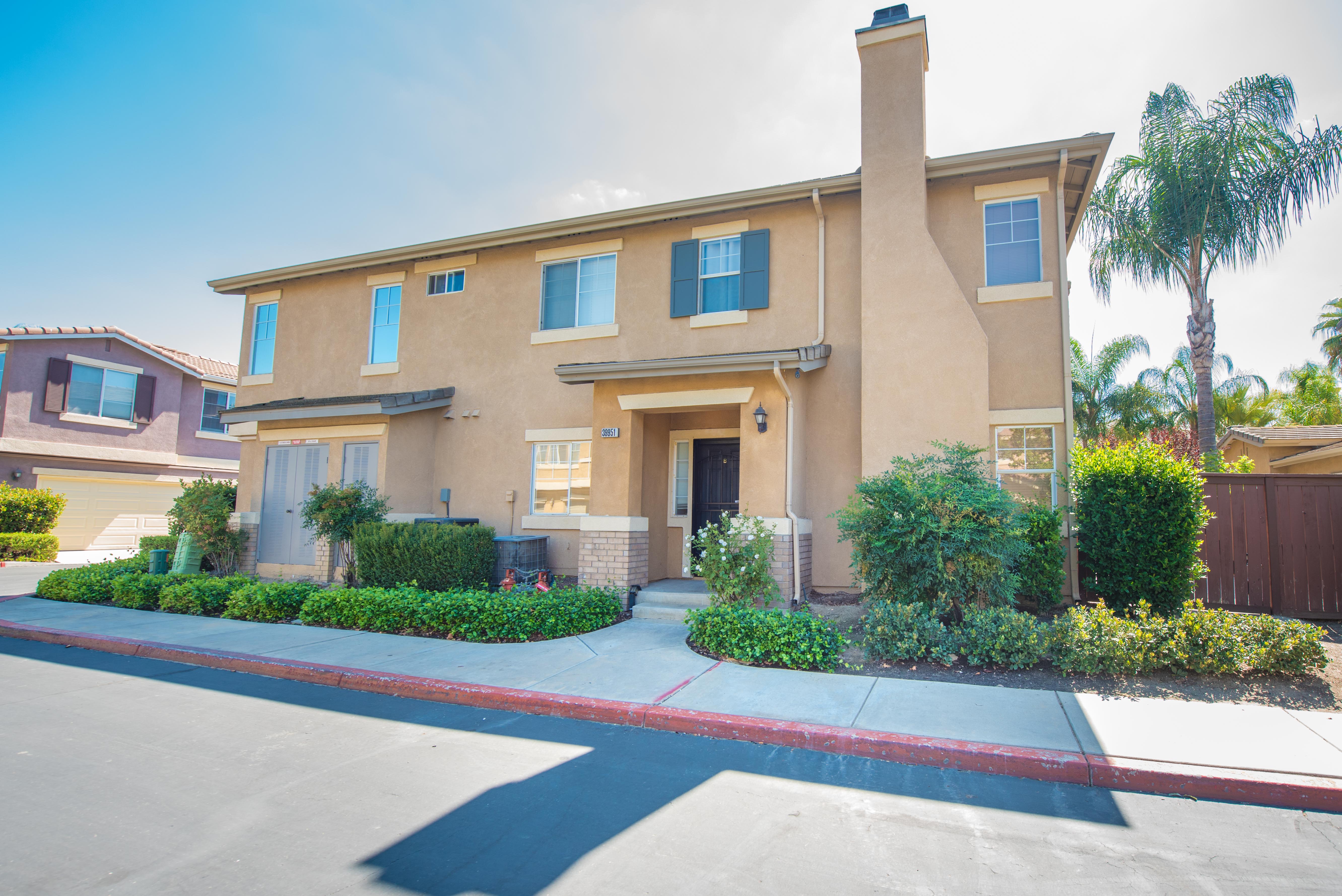 Front exterior of 39951 Millbrook Way #B in Murrieta, a two-story home with tan stucco exterior, landscaped walkway and covered entry.