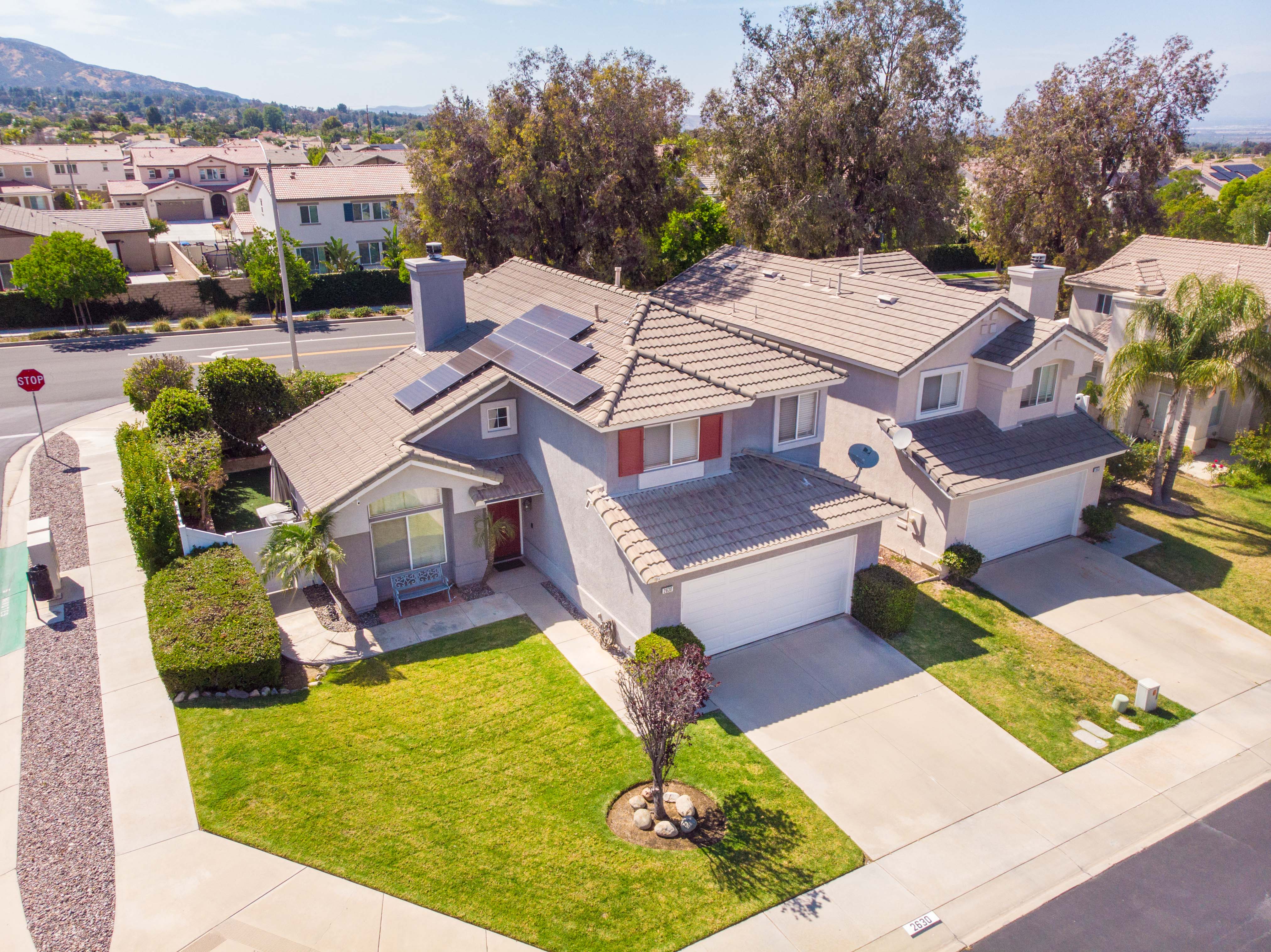 Aerial exterior view of two-story home at 2630 Galisteo Street in Corona, California, featuring rooftop solar panels, attached two-car garage, landscaped front yard, and surrounding residential neighborhood.