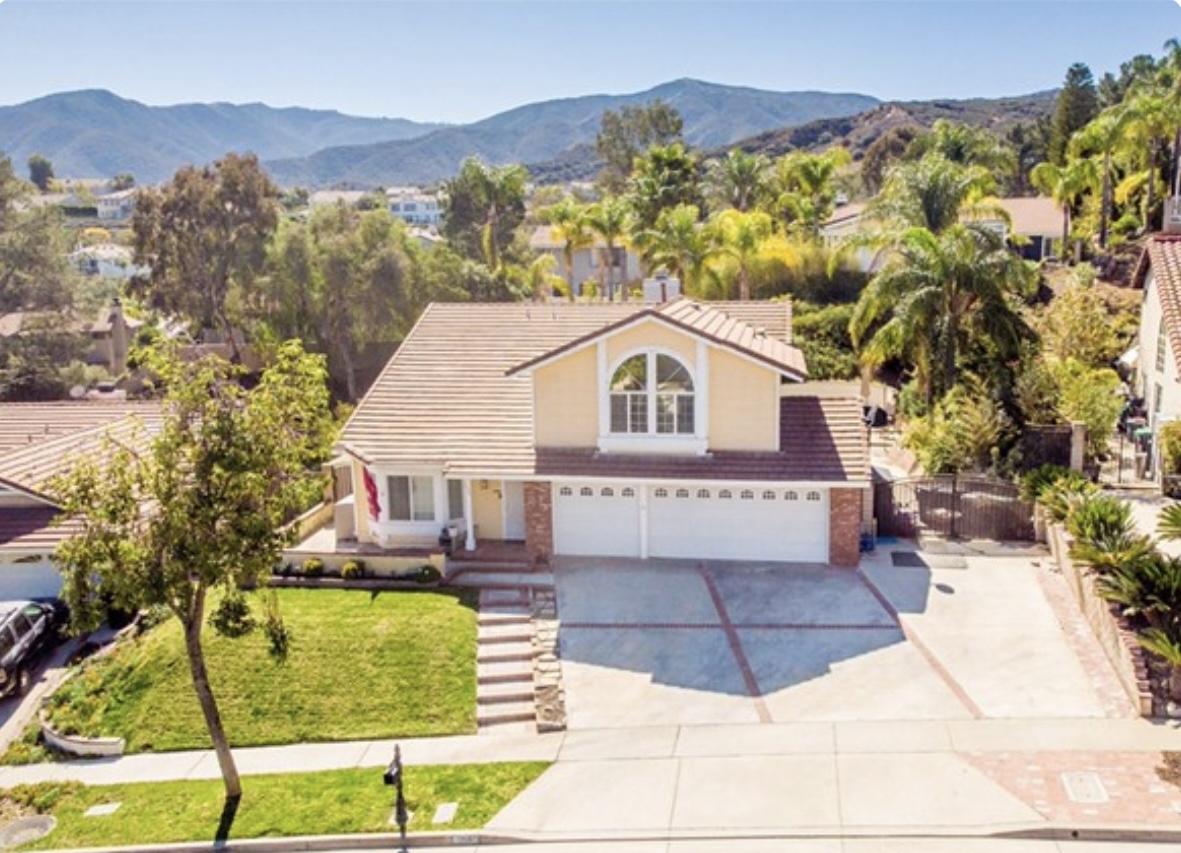 Aerial view of a single family home with 2 car garage in a Corona California residential neighborhood with mountains in the background.
