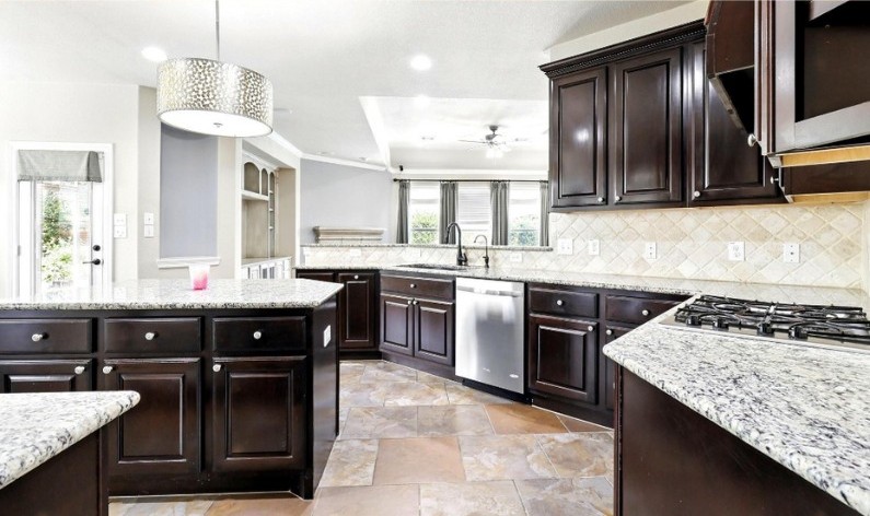 Spacious modern kitchen with dark wood cabinets, granite countertops, stainless steel appliances, and tile flooring in a Houston home.
