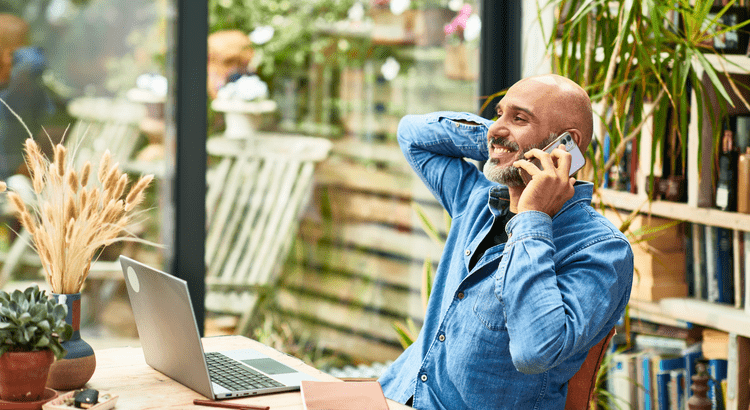 Person working remotely on a laptop with a home for sale in the background