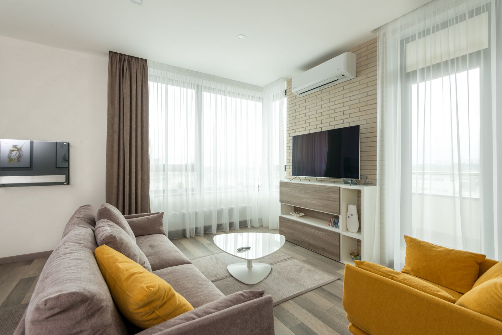 Bright furnished living room with gray sofa, yellow armchair and wall-mounted TV - preparing a New Hampshire home for sale and seller disclosure