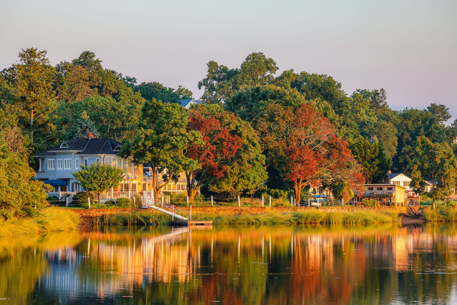 Gray New England home beside a calm river with early-fall maples at golden hour - New Hampshire property taxes by town