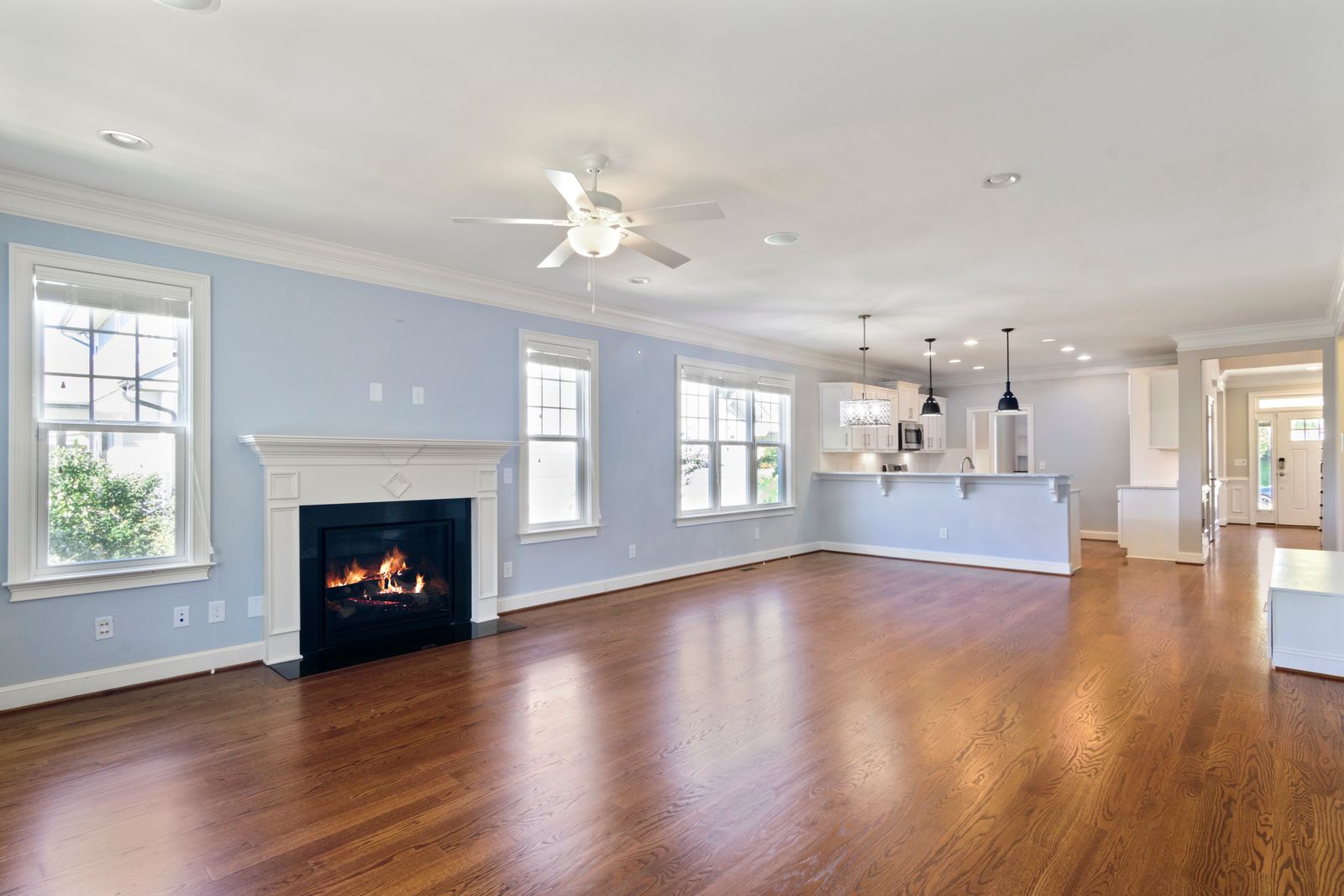 Empty, cleared-out living room with a fireplace, hardwood floors and an open kitchen - an inherited New Hampshire home readied for sale