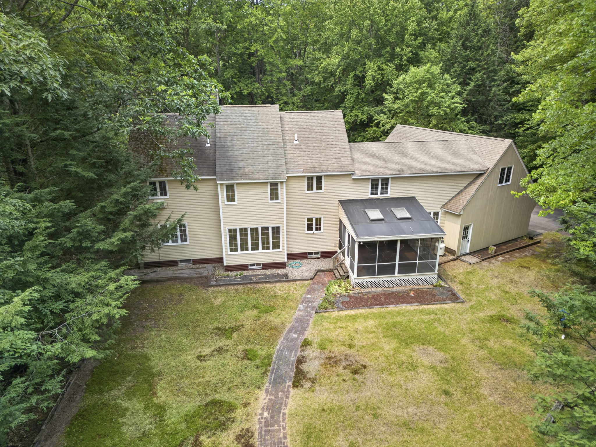 Aerial summer view of a cream colonial home surrounded by green New England woods in Bedford NH, illustrating who pays the buyer agent fee when buying a home