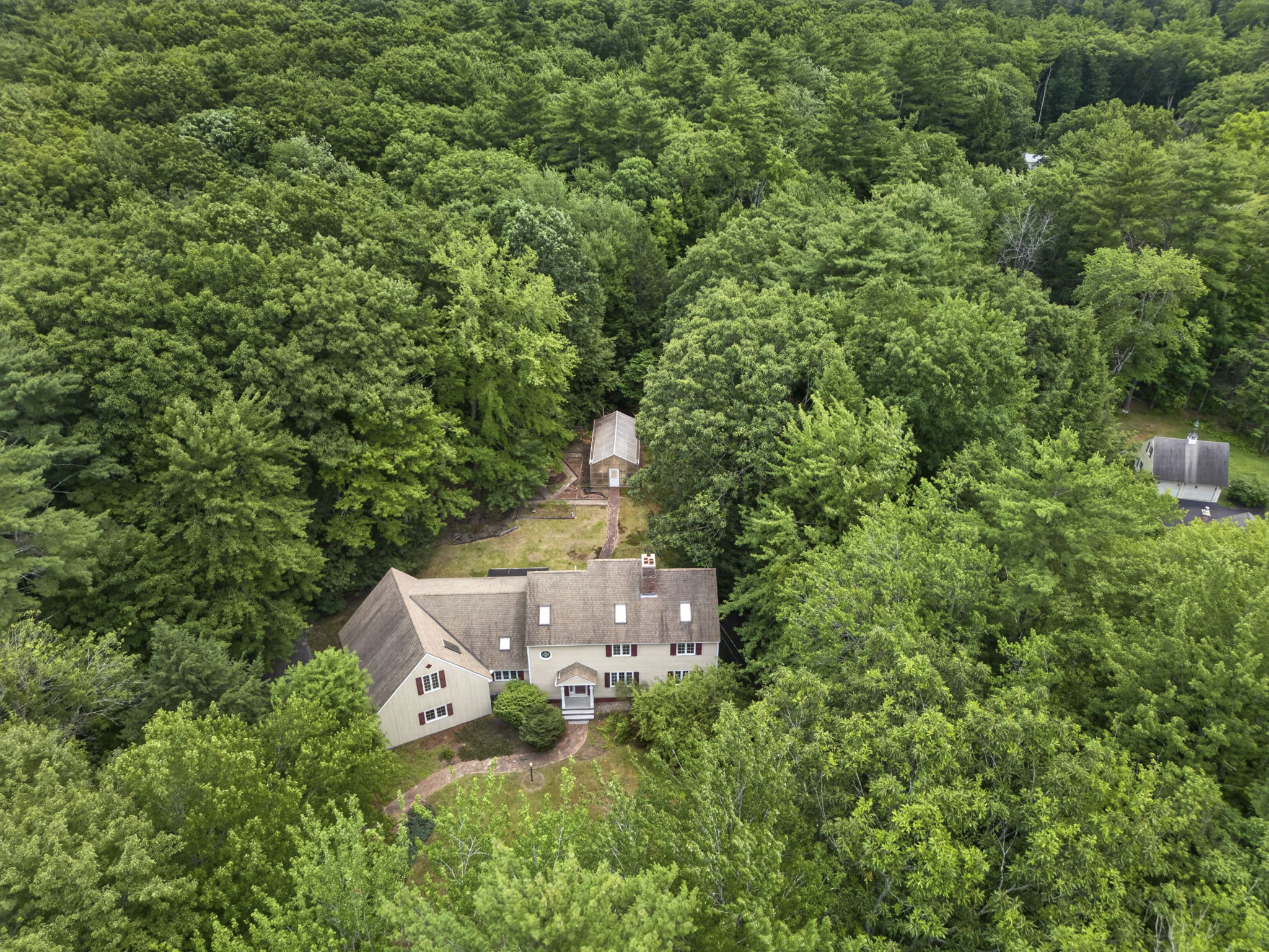 Aerial summer view of a classic cream New England colonial home with red shutters on a wooded Bedford NH lot, symbol of buying a home in New Hampshire