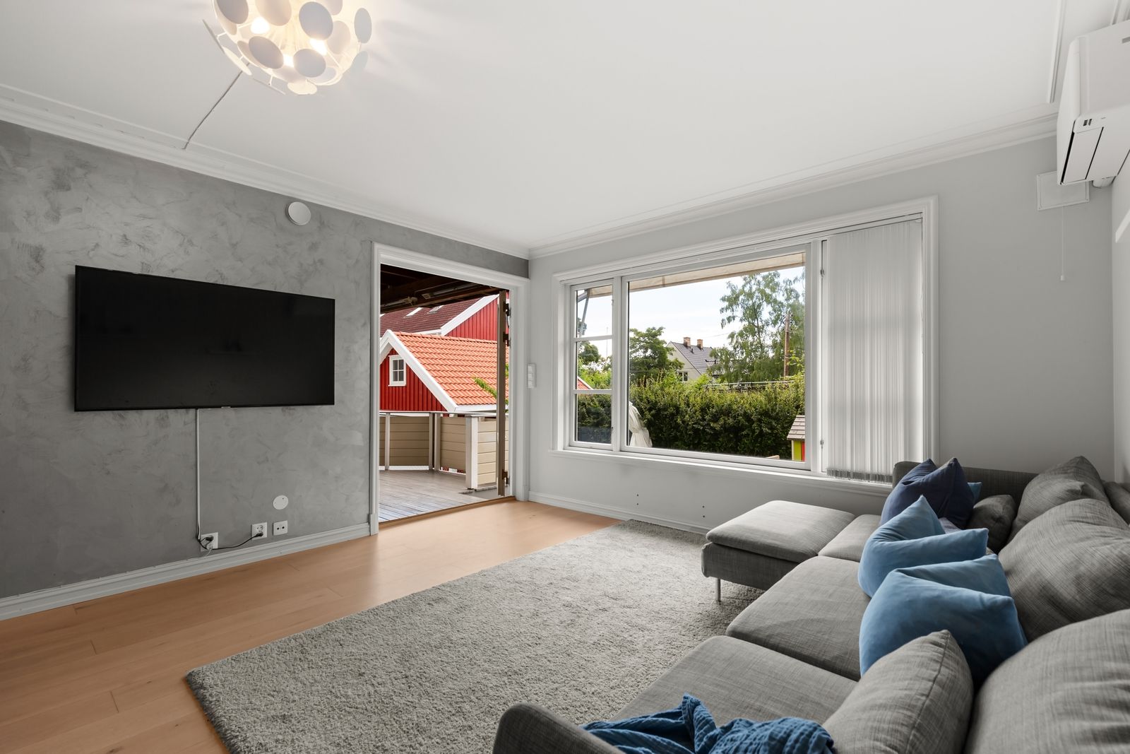 Lived-in living room with a gray sectional, wall-mounted TV and sliding door to a deck - a New Hampshire home shown in its current condition
