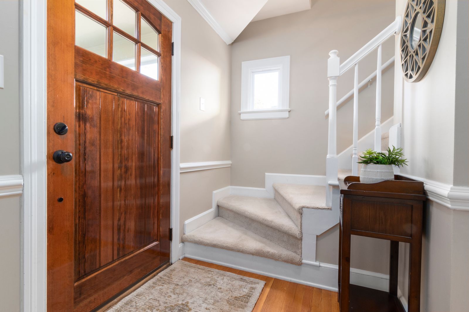 Home entry with a wood front door, small window, white staircase and wood side table