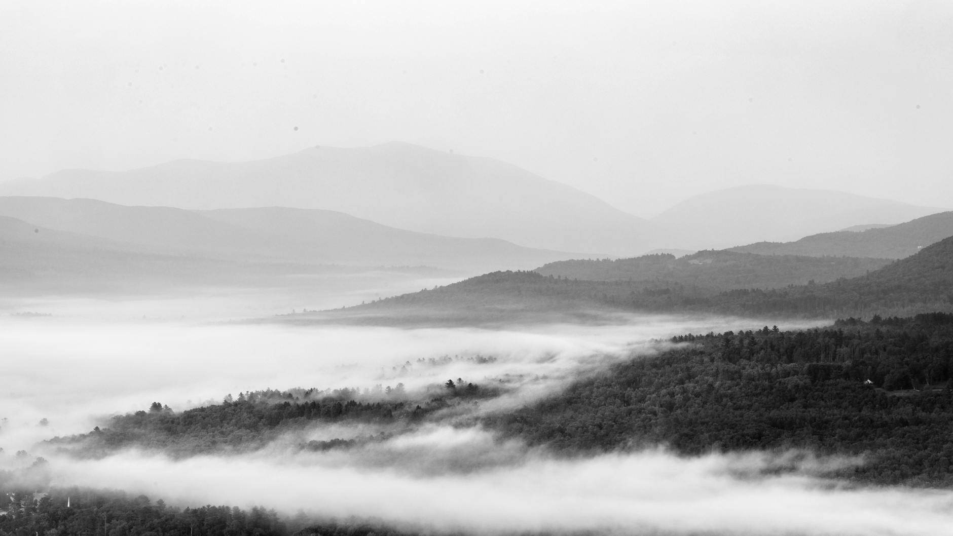 Early-morning fog drifting over forested New Hampshire hills in black and white — the quiet rural landscape surrounding Hollis school communities
