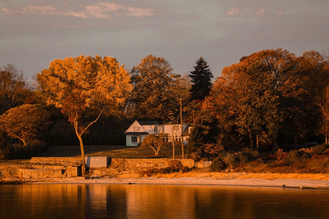 Small white New England cottage among golden autumn trees on a pond shore at sunset, Derry NH ADU guide