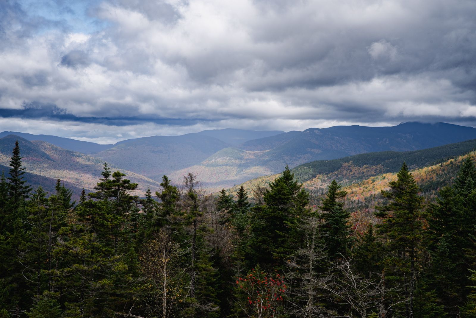 Early-fall foliage across a New England mountain valley under moody clouds - the landscape people keep when moving to NH from Maine