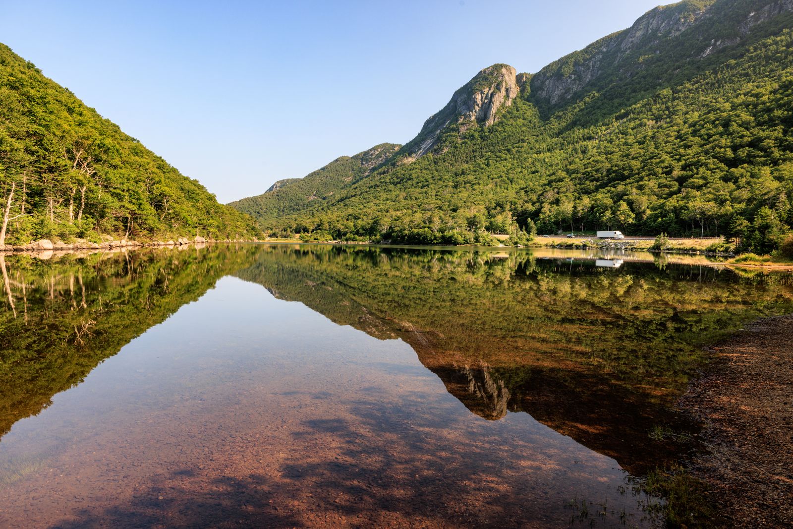 Calm summer morning on a New England mountain lake with forested slopes and a cliff face reflected in the water - moving to NH from Connecticut