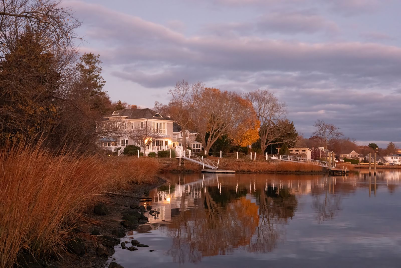 Large white New England home with a porch on a tidal river at autumn sunset, marsh grass in the foreground - the kind of home buyers are chasing in New Hampshire's fastest growing towns