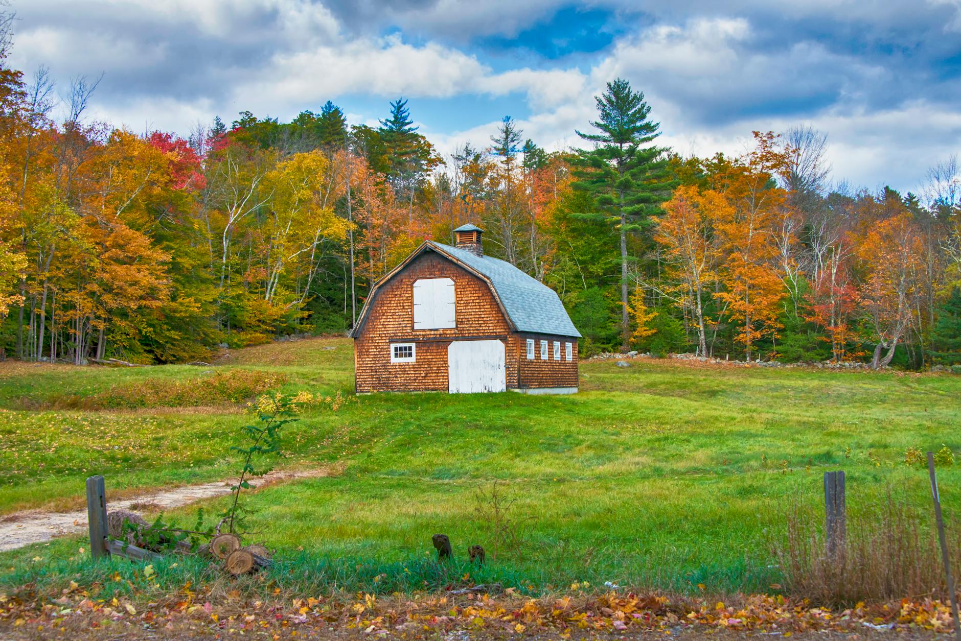 Classic New England shingle-sided gambrel-roof barn in a grassy field framed by autumn trees, the kind of outbuilding a Manchester NH ADU conversion can transform