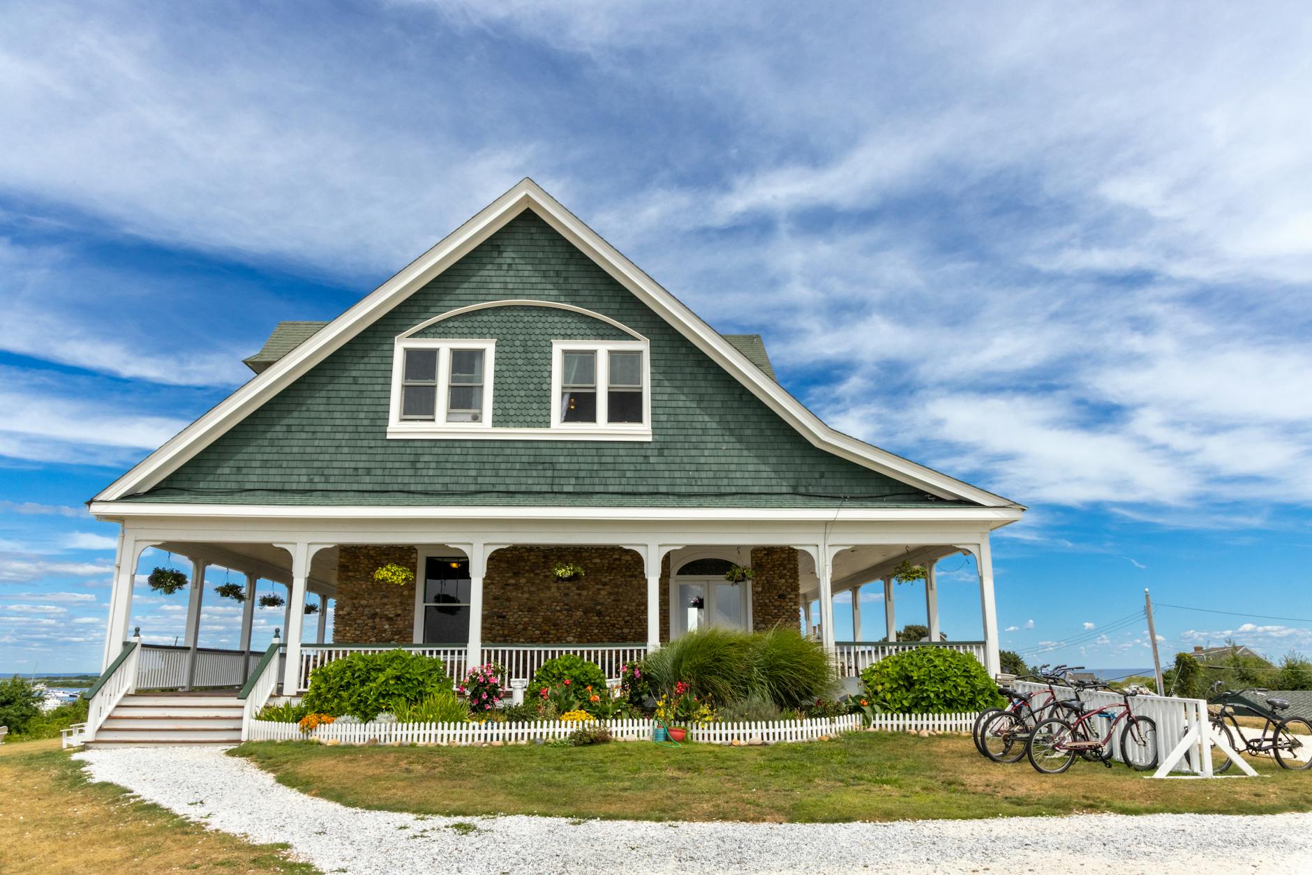 Green shingle-style New England home with a white wraparound porch and summer flower gardens, the kind of home buyers inspect before closing in New Hampshire